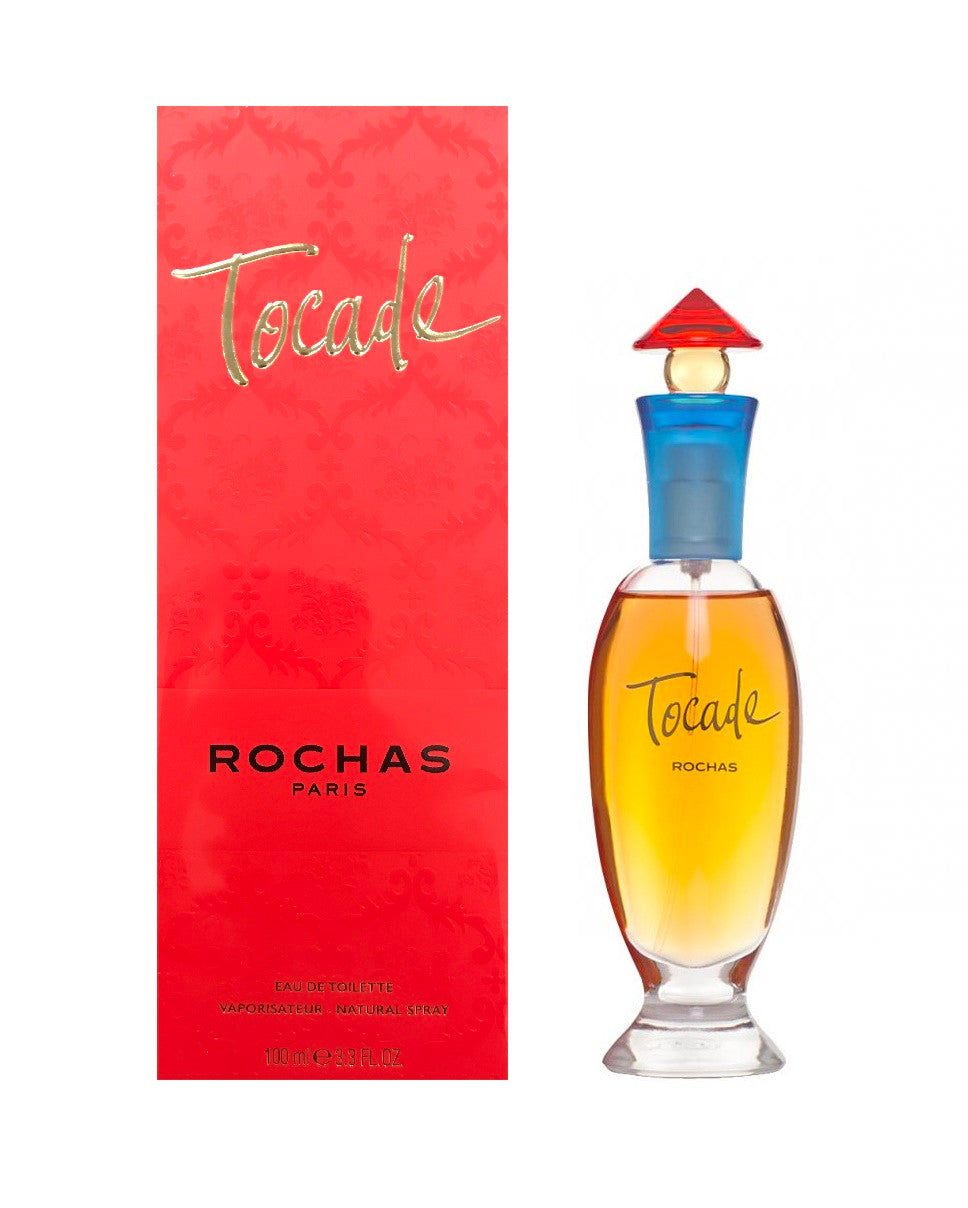 A product image featuring TOCADE EAU DE TOILETTE SPRAY by ROCHAS. The image shows the perfume bottle with a red cap on a white background, accompanied by its red packaging box.