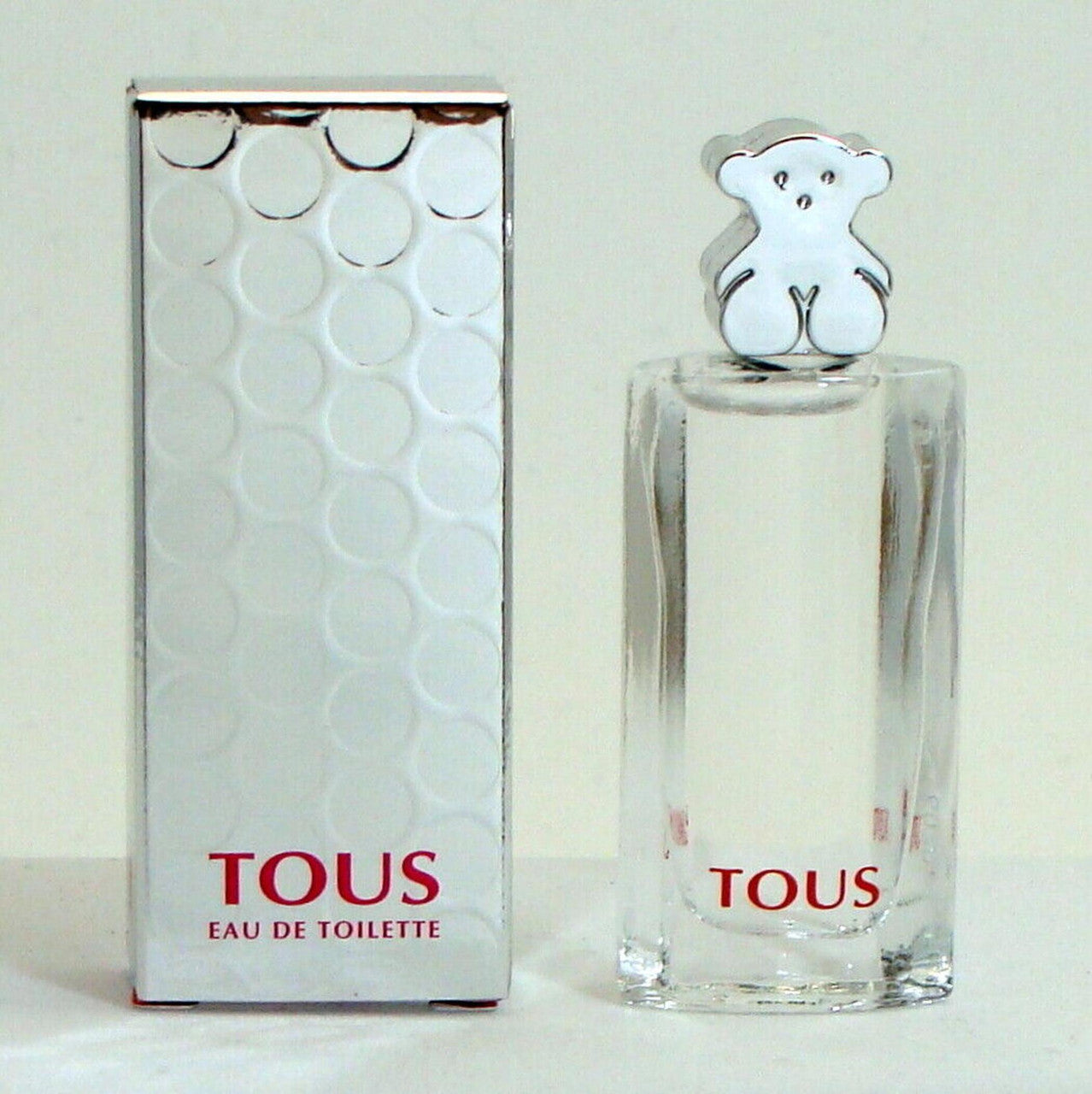 A sealed box of TOUS brand eau de toilette for women alongside a clear glass bottle with a silver cap, both displaying the brand name 'TOUS'.
