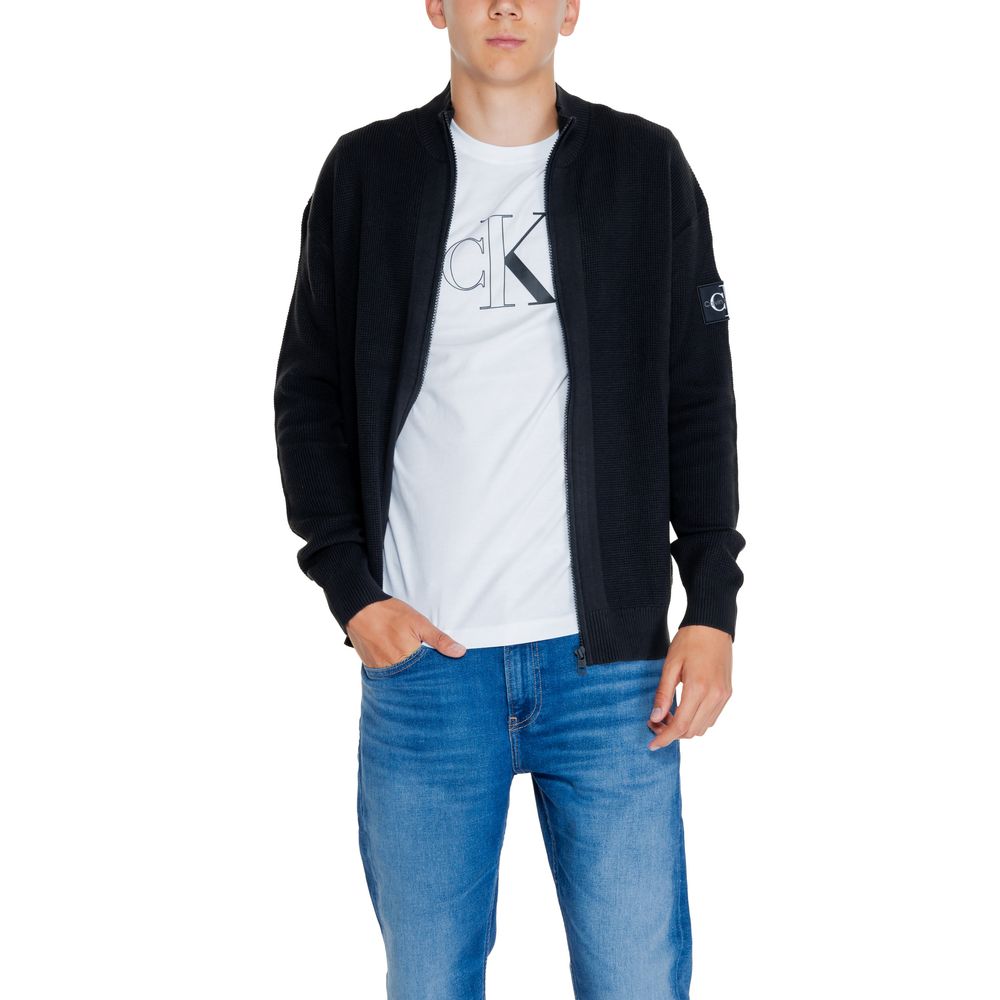 Man in Calvin Klein Jeans Black Cotton Rigenerato Cardigan, white t-shirt, and blue jeans